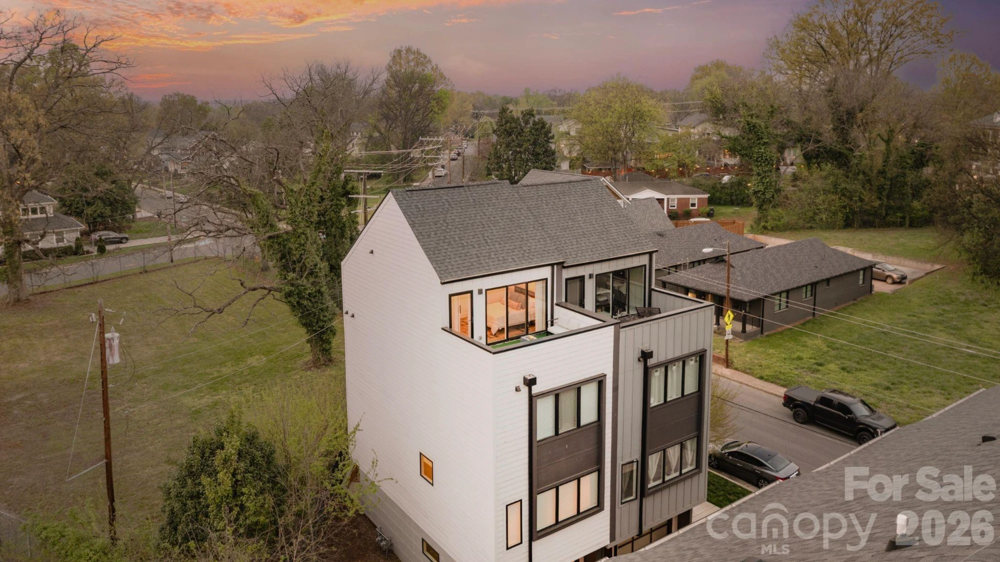 Aerial dusk photograph of the four-story townhome exterior showing the full elevation, rooftop terrace, and surrounding neighborhood tree canopy