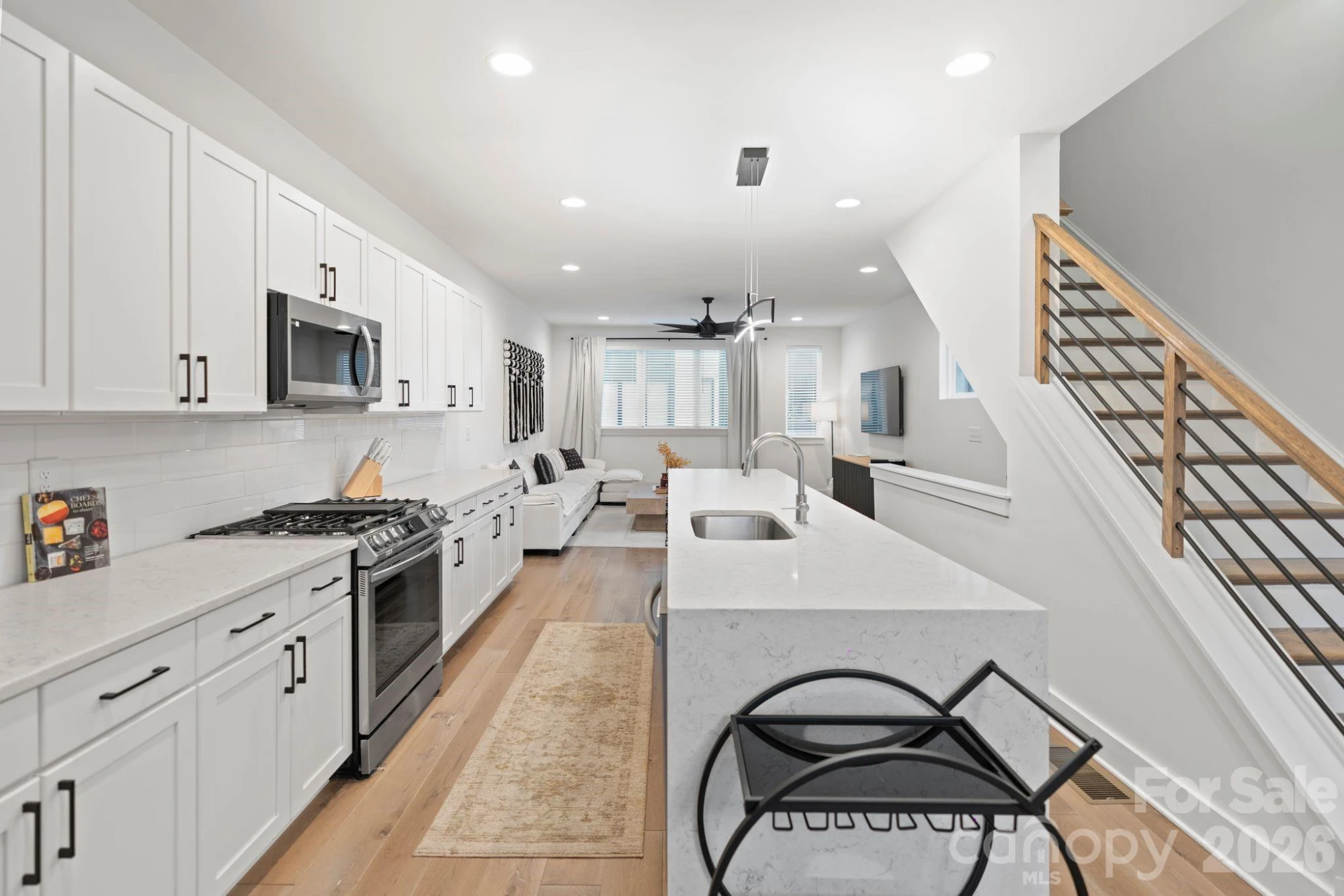 Open-plan living room and kitchen with white shaker cabinetry, quartz waterfall island, gas range, and wide-plank hardwood floors