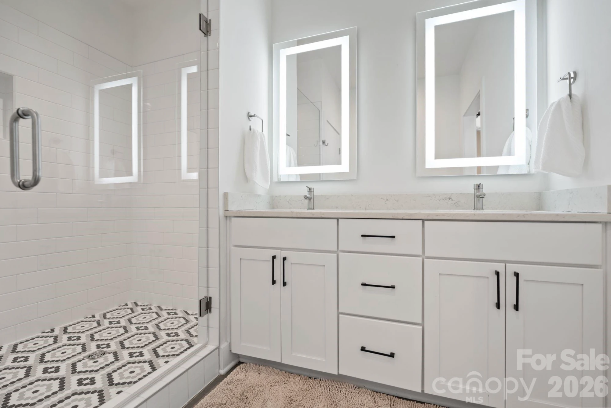 Primary bath with double quartz vanity, backlit LED mirrors, and a glass walk-in shower with patterned mosaic tile floor