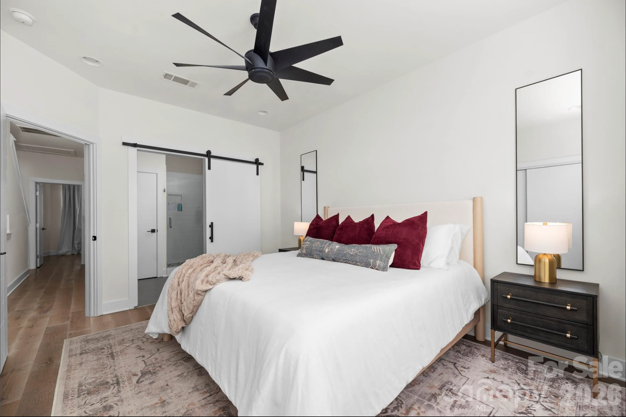 Primary bedroom with king bed, black ceiling fan, barn-door en-suite bath, and wide-plank hardwood floors
