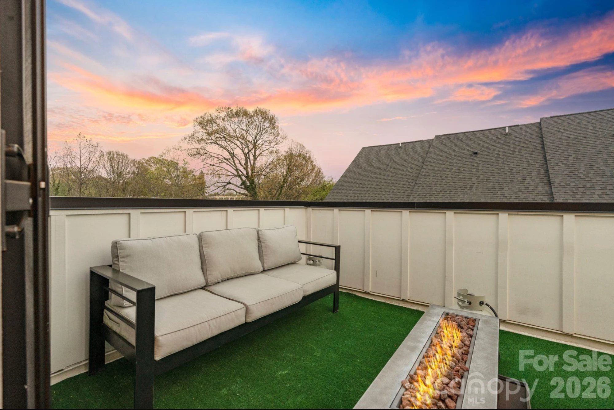 Private rooftop terrace at sunset with outdoor sofa, linear gas fire pit, and open sky views