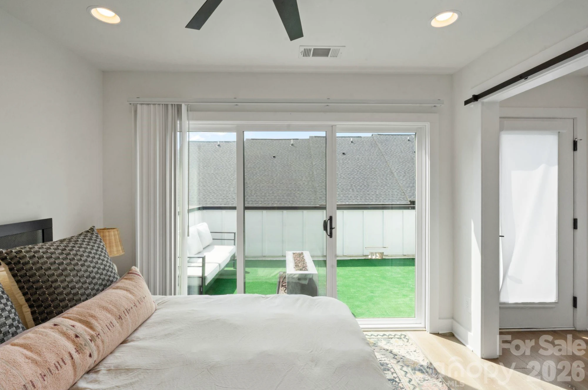 Primary bedroom with black metal bed frame and patterned pillows, floor-to-ceiling sliding glass doors opening directly onto the rooftop terrace